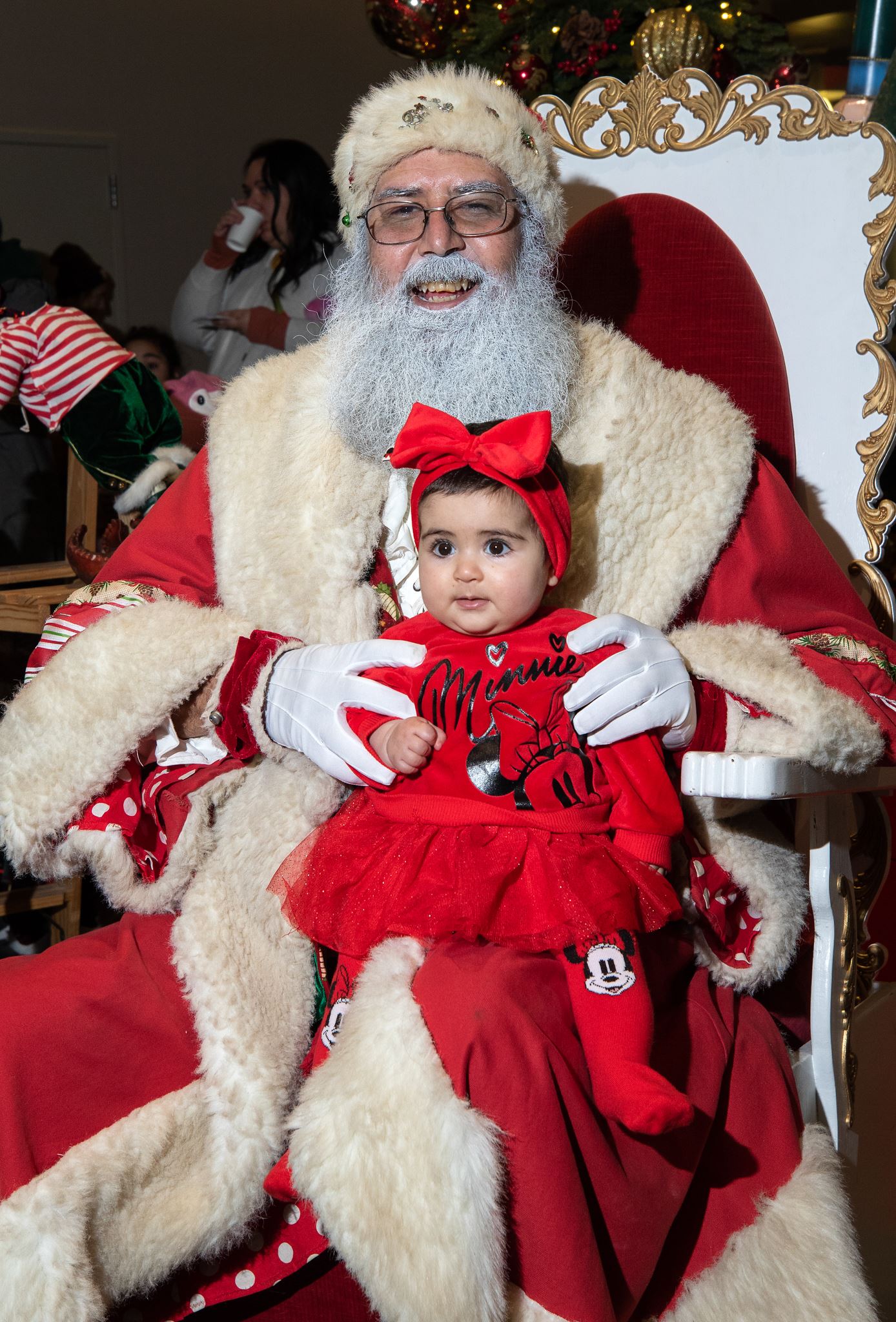 Santa with a tiny tot all dressed in red that includes a big red bow on her head