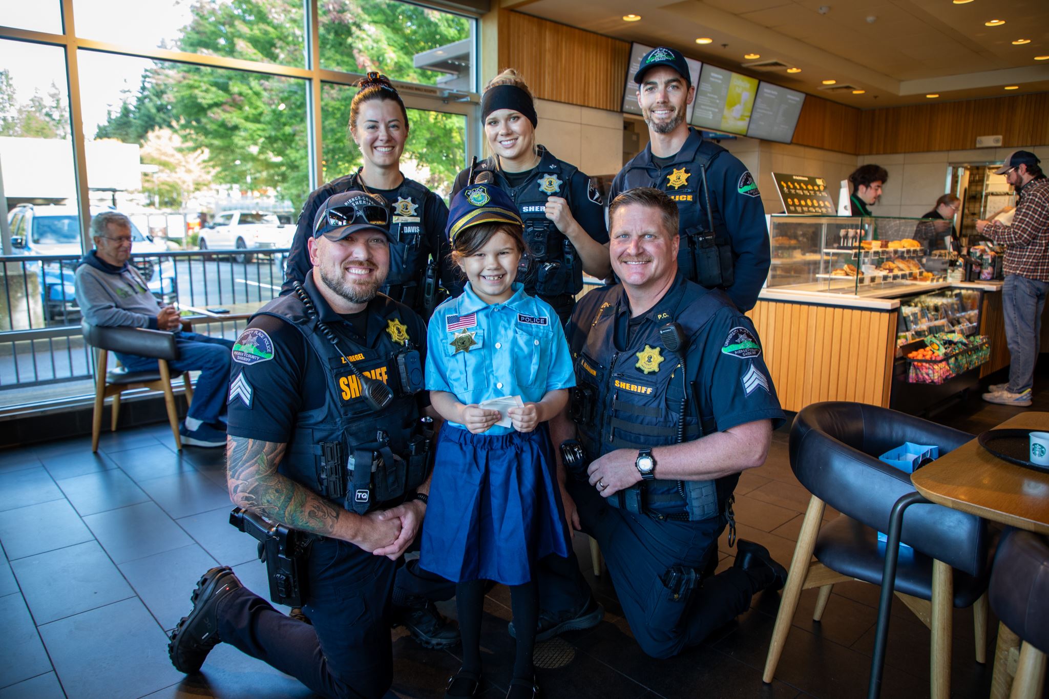Group of police posing for photo with young girl wearing police uniform costume